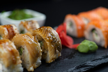Sushi set with roll eel and salmon and hayashi wakame salad lie on a black board made of slate stone