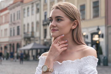 Gorgeous young model girl with perfect blonde hair looking at camera posing in the old city wearing white dress.