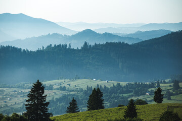 Beautiful summer Carpathian mountains, at early morning, just before sunrise. Beautiful sunrise over mountain foggy valley. Haystack on grassland hill on foreground.
