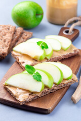Sandwich with whole grain cracker, green apple slices and peanut butter, on  wooden board, vertical
