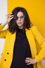 stylish and daring young brunette in a bright yellow jacket and mirrored sunglasses.