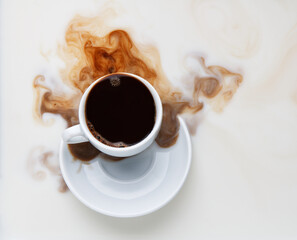 black coffee pouring from a white cup into milk