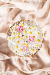 Tender floral aesthetic. Creative summer image with space for text. Bohemian mood. Wildflowers in water in stylish wine glass on background of soft beige fabric. Top view