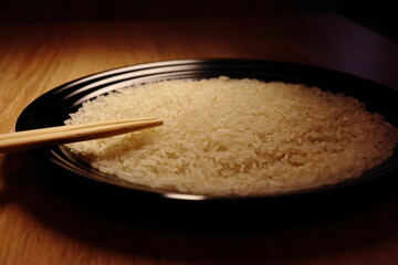 Raw white rice and sticks on the black plate. Close up view. Isolated on wooden background. Food photography.