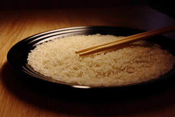 Raw white rice and sticks on the black plate. Close up view. Isolated on wooden background. Food photography.
