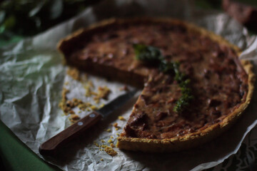 Mushroom quiche on baking paper. Small knife. Basil flowers on the pie. Dark photo