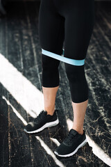Close-up of a woman's leg in black leggings who pumps leg muscles using a blue elastic expander on the hips in a loft