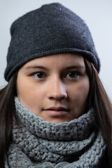 Young lady poses for an extreme closeup portrait. She is caucasian in her 30s. She is wearing a gray scarf and a blue hood. She is serious.