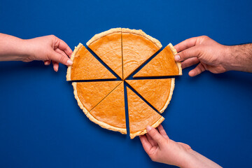 Sliced pumpkin pie above view on blue background. People grabbing slices of cake