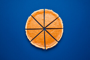 Sliced pumpkin pie top view isolated on classic blue background. Homemade cake. © YesPhotographers