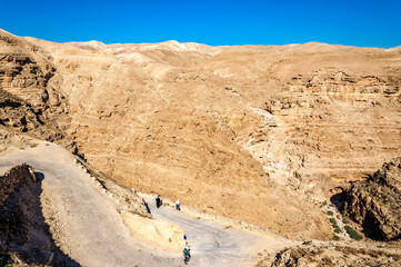 Hills and gorge Wadi Kelt in the Judean desert near the monastery of St. George Hosevit (Mar Jaris). Pilgrims go along the road leading to the monastery. Palestine, Israel.