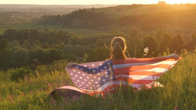 Happy woman with USA national flag outdoors at sunset. Positive girl celebrating United States independence day. International day of democracy concept.
