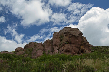 Rocky formation at the top of the hill. The meadow and vegetation under a beautiful blue sky with clouds. 