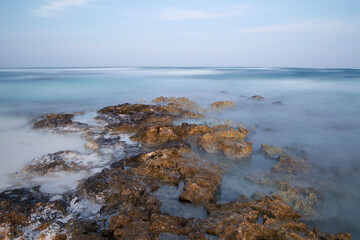 Long exposure shot of the ocean water and shore at sunset. Dreamy view of the blurred sea waves and rocks with magical twilight colors.