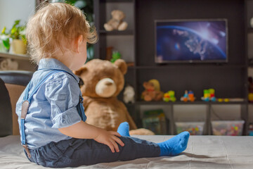Cute baby boy watching TV sitting on a couch in the living room at home