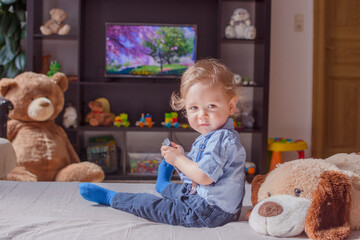 Cute baby boy and his dog plush toy watching TV sitting on a couch in the living room at home