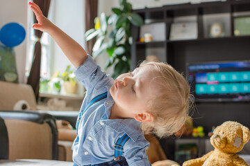 Cute baby boy and his teddy bear playing in front of the TV on a couch in the living room at home