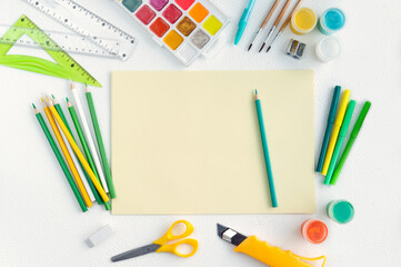 Blank yellow sheet of paper with colored school supplies