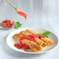 Three delicious crepes on a plate covered with strawberry sauce poured from a spoon, light grey background