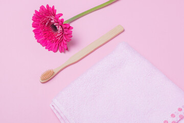 Eco-friendly bamboo toothbrush and flower on pink background. Natural organic bathroom beauty product.