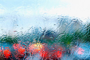 Blurred mode of transport through windshield on a rainy cloudy day. Heavy rain, raindrops on the windshield, blurred cloudy background from a car window.