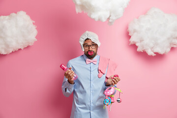 Future father poses with diaper on head, feeding bottle and mobile in hands, awaits for baby birth,...