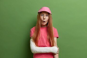 Children, face expressions concept. Surprised freckled girl looks with wonder at camera, has broken...