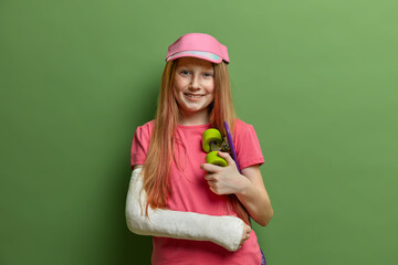 Smiling redhead girl had accident after riding skateboard, wears cast or plaster on broken arm,...
