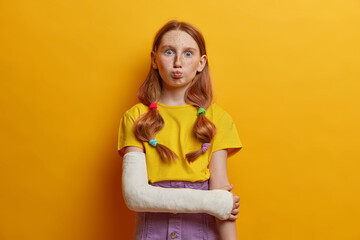 Lovely schoolgirl makes funny expression, pouts lips, has two pony tails, red hair, freckled face,...