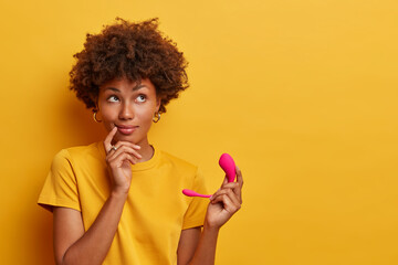 Pensive dark skinned model holds waterproof G spot vibrator on remote app control for getting...