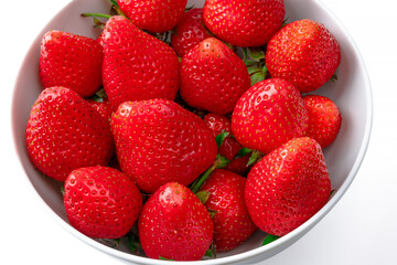 Many sliced vivid red strawberries in white porcelain bowl on isolated white background. Copy space for text or banner