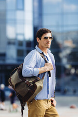 Portrait of handsome confident fashionable male model wearing sunglasses carrying backpack in city