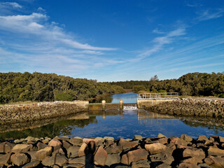 Beautiful view of a mini waterfall onto a pond in a nature reserve with reflections of blue sky, light clouds and trees on water, Newington Nature Reserve, Sydney, New South Wales ,Australia