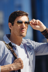 Cheerful handsome fashionable free male dressed in blue shirt and wearing sunglasses