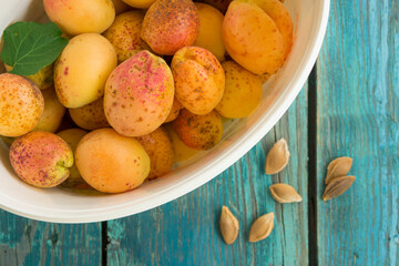 Large ripe yellow apricots, green leaves and seeds from apricots on a green wooden background