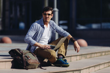 Stylish confident fashionable male sitting and holding notebook and looking straight in the camera