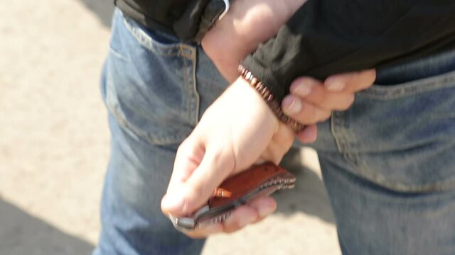 A man takes the pocket knife out of his jeans and secretly opens it, standing outdoors, also in his car
