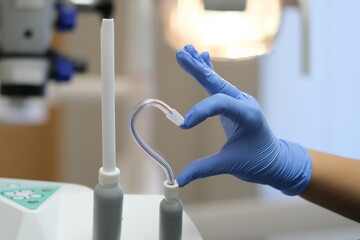 Hand in Blue latex glove and saliva ejector in shape of heart and dental microscope on beckground