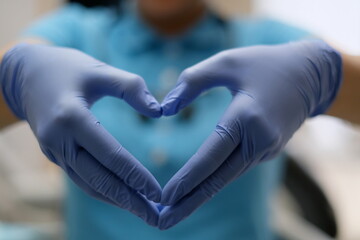 Nurse hands in Blue latex gloves in the shape of heart against the background of her body in Blue shirt