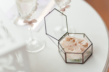 Wedding rings in the glass box filled with roses standing on the white table. Wedding accessories