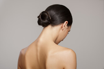 brunette with a smooth bun hairstyle from the back. on gray background - obrazy, fototapety, plakaty