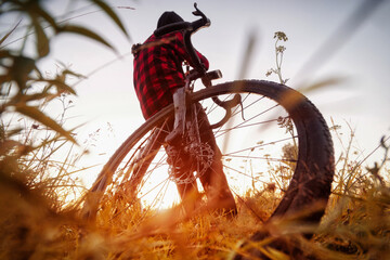 Man with bike in the field. Wide angle view of a cyclist sitting on his bicycle at sunrise in a...