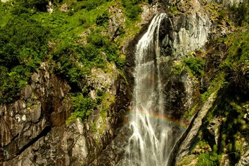 Top view of a beautiful waterfall on the mountain rock on a sunny summer day with a rainbow.