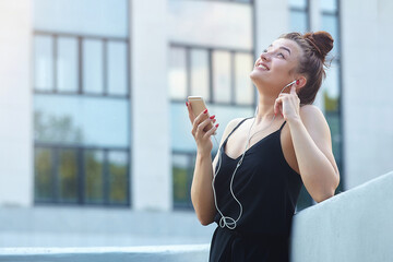 Fototapeta premium beautiful girl poses in the city, holding a smartphone and listening to music with headphones