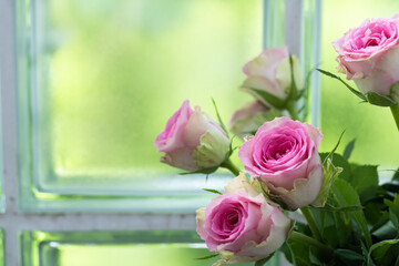 Bouquet of pink roses in a vase against a window background