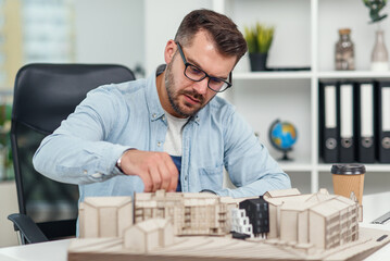 Handsome caucasian senior architect at glasses working on a construction project and examines the model on which he works.