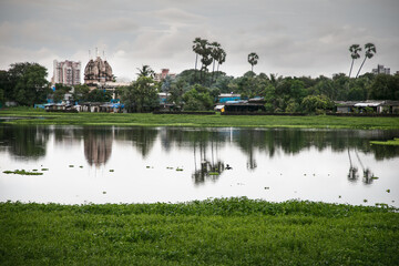 Landscape Wide angle shot of the buildings temple and colony with the reflection in the rain water pond and green coconut tree boys fishing with stick in Mumbai Maharashtra India on 27 July 2020