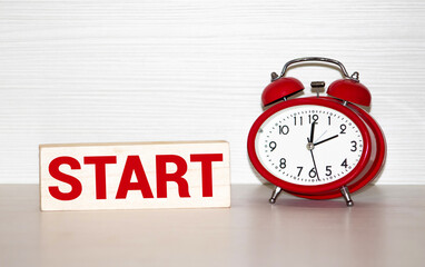 Red alarm clock and wooden cubes with START word on table with blurred green background.