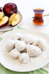 Apple cookies with powdered sugar in plate on the white surface with a cup of tea.
