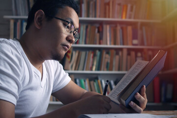 Young Asian man studying in library, exam preparation concept. Male college student doing research and making notes in his book